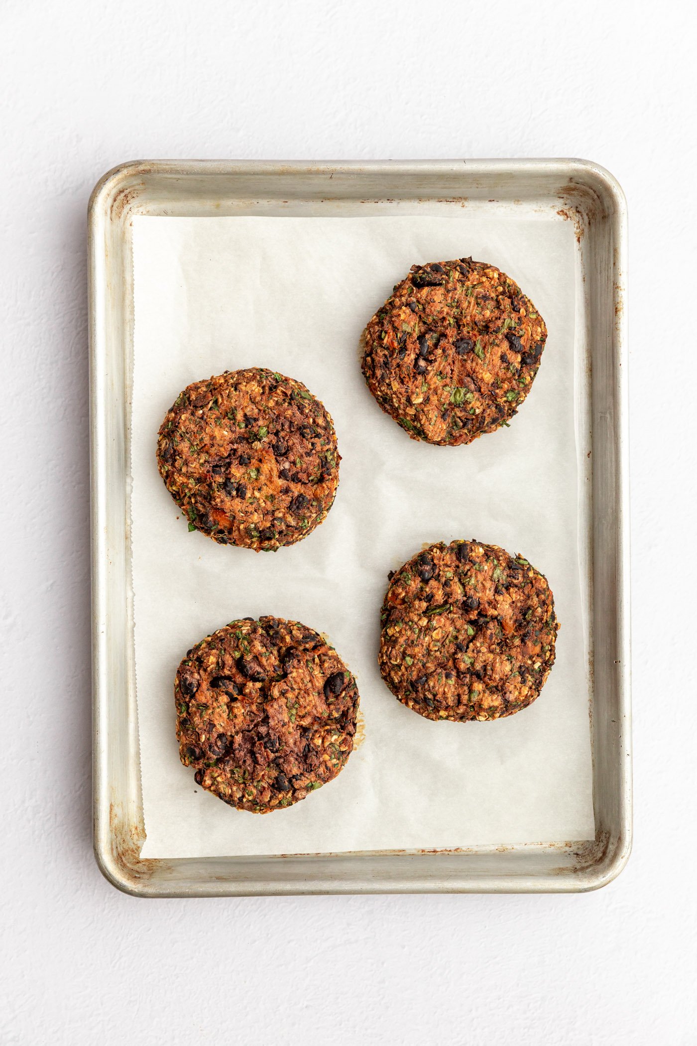 4 black bean sweet potato veggie burger patties on a lined baking sheet after being cooked.